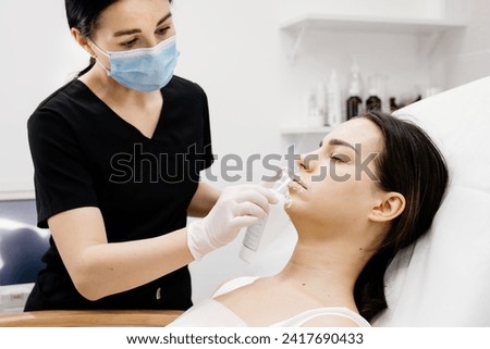 Cosmetology clinic, the doctor applies anesthesia to the patient's lips, anesthetic before injecting hyaluronic acid. Anesthetic ointment is applied before the injection procedure. Royalty-Free Stock Photo #2417690433