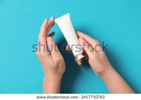 Woman with tube of hand cream on light blue background, top view
