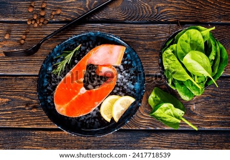 Fresh raw salmon fish fillet with cooking ingredients, herbs and lemon on black background, top view