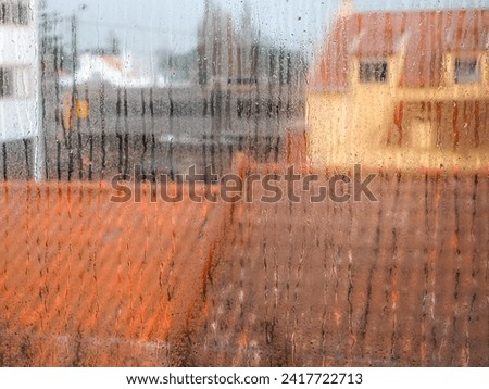 Surface of wet dirty glass. Blurred image, window with rain droplets and city houses with orange tiled roofs visible through them. Textured surface pattern, colorful design texture.