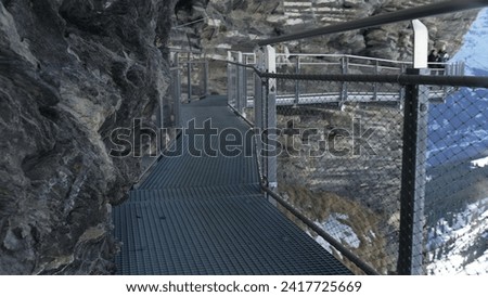 Metal pathway on side of mountain cliff, Grindelwald First Mountain trail pathway supported by elevated metal walkthrough in Swiss Alps Royalty-Free Stock Photo #2417725669
