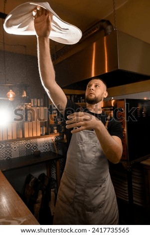 Man in uniform making a pizza dough. Cook twirls a round pizza base in his hand in the kitchen