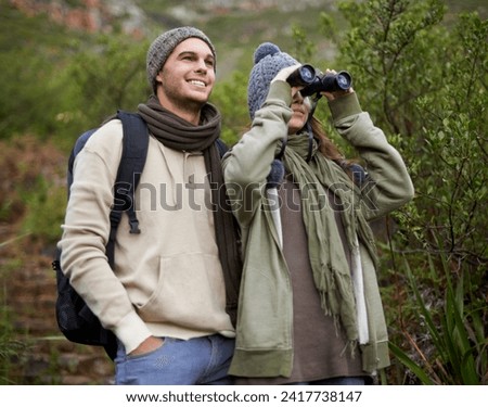 Couple, travel and binoculars in nature for hiking, adventure and journey or explore together in winter. Happy man and woman trekking with outdoor search, vision or birdwatching in forest or woods Royalty-Free Stock Photo #2417738147