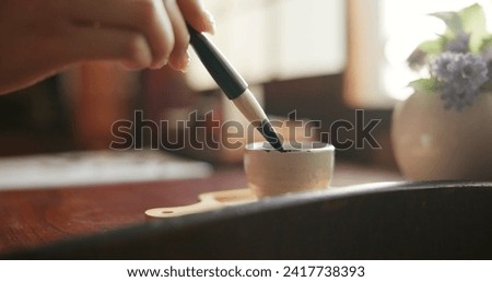 Brush, closeup and hands at a table for calligraphy, writing or ancient Japanese art in a house. Letter, communication and zoom on person fingers with traditional ink stroke, penmanship or art tool Royalty-Free Stock Photo #2417738393