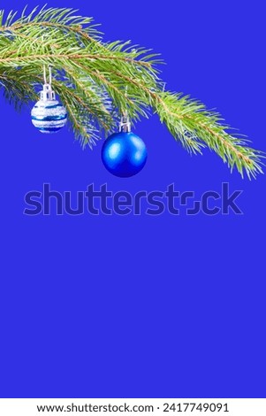 A spruce branch with Christmas tree decorations on a bright blue background. Ideal for a New Year's card or invitation.