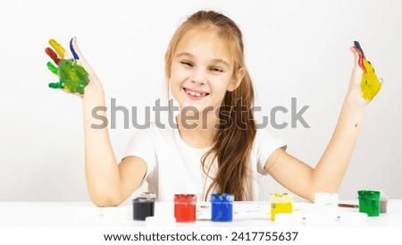 Art drawing for children. A child girl on at table indoors with her hands stained in paint.