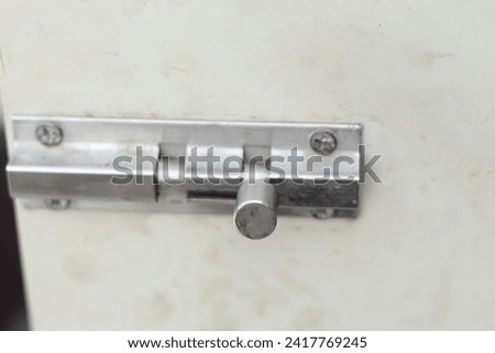 The barrel bolt or door knob or bolt made of stainless steel, which is a rust-resistant and durable material. It has a rectangular shape with rounded corners on white door, dirty
