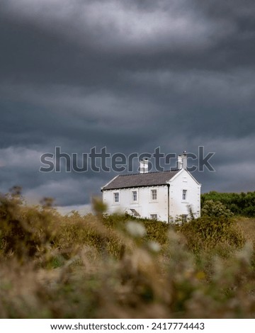 Stunning white cottage near a beach under dramatic storm clouds - Former lighthouse keepers house at Penmon Point North Wales Royalty-Free Stock Photo #2417774443