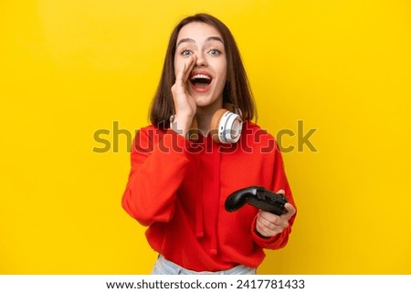 Young Ukrainian woman playing with a video game controller isolated on yellow background shouting with mouth wide open