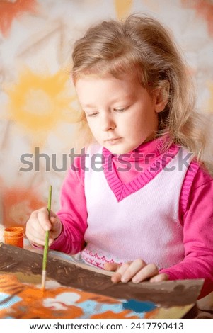 cute baby girl with blond hair is engaged in drawing