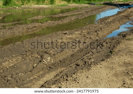 gutter on the village road after heavy rain with tractor traces Royalty-Free Stock Photo #2417791975