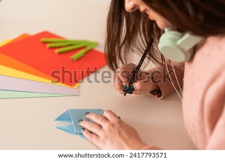 Close-up of a focused woman adding details to a blue origami fish, a potential playful gag for April Fools' Day.