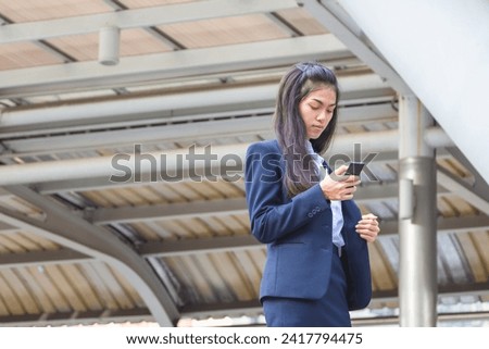 Young Asia woman using smartphone standing on the city street, Asian businesswoman reading news on smartphone while walking outdoor