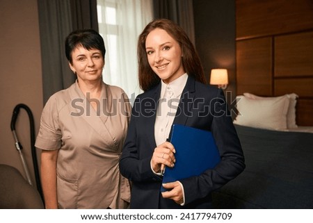 Smiling housekeeping manager checking maid work during room cleaning procedure Royalty-Free Stock Photo #2417794709