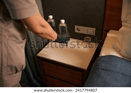 Maid placing two bottled drinks on bedside table in hotel room Royalty-Free Stock Photo #2417794807