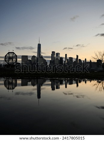 Downtown new york city with freedom tower and jersey city clock reflected in a puddle