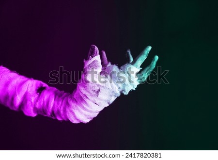 Mummy hand wrapped in a bandage in neon light. Halloween concept