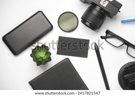 Black business card on a white background with a camera, notepad and modern accessories and gadgets on a white background