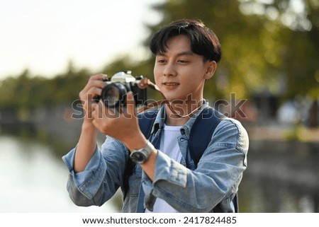A Handsome backpacked male tourist taking a photo with a film camera at Chiang Mai moat on the background, Solo travel concept.
