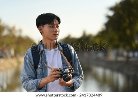 Portrait of A Handsome male tourist holding a film camera at Chiang Mai moat on the background with copy space, Solo travel concept.