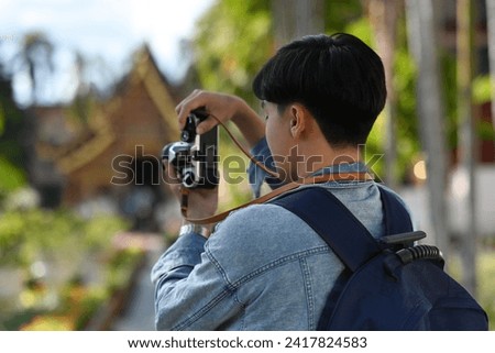 Rear view image of A handsome Young Asian traveler man taking a picture of a beautiful Thai Temple with his film camera, Thailand traveling and Solo traveler concept.