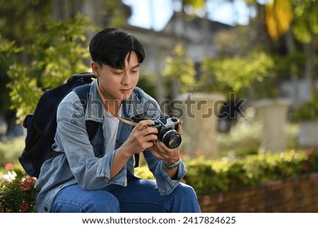 A handsome Young Asian traveler man sitting and looking a picture from the camera while visit a beautiful Thai Temple, Solo traveler concept.