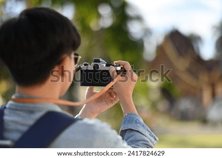Rear view image of A Young Asian traveler man taking a picture of a beautiful Thai Temple with his film camera, Thailand traveling and Solo traveler concept.