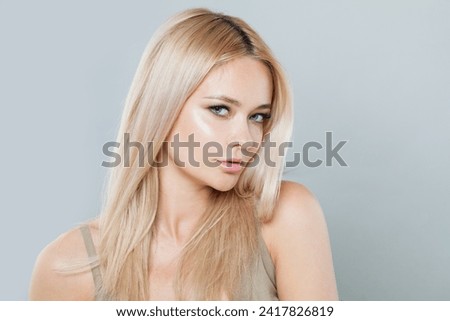 Joyful blonde woman with long straight hair and clean fresh pure perfect skin isolated on gray background, studio portrait