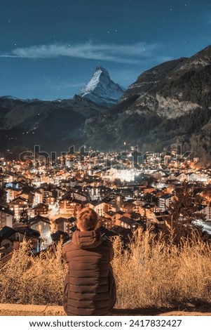 Rear view of man sitting and enjoying the view of illuminated Zermatt village and Matterhorn mountain in the night at Switzerland