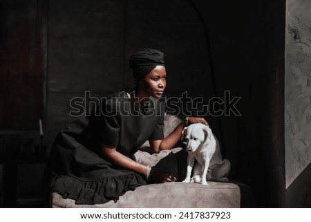 Contemplative African woman with her dog in a serene, shadowy room Royalty-Free Stock Photo #2417837923