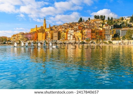 A small group of sailboats pass in front the old town and Les Sablettes Beach and promenade along the Cote d'Azur French Riviera at Menton, France. Royalty-Free Stock Photo #2417840657