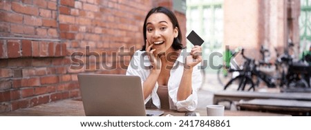 Portrait of young stylish girl sits near laptop, shows credit card and smiles, pays bills, shops online. shopping and mobile banking concept