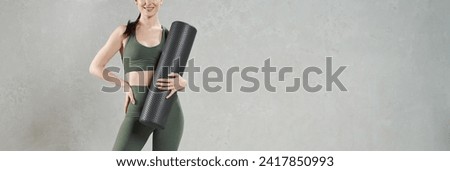 Unrecognizable female athlete posing, while holding dark mat for yoga practice. Crop view of brunette woman in sport outfit standing with hand on waist and smiling, copy place. Sport, fitness concept.