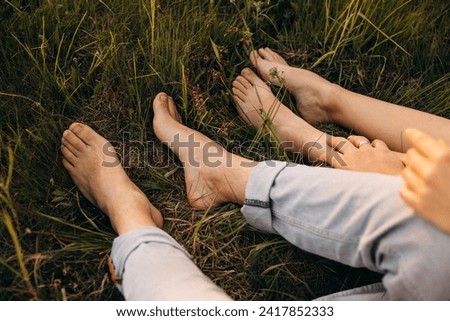 Bare feet of boy and girl sitting on grass hugging photo close up. Walking barefoot Royalty-Free Stock Photo #2417852333