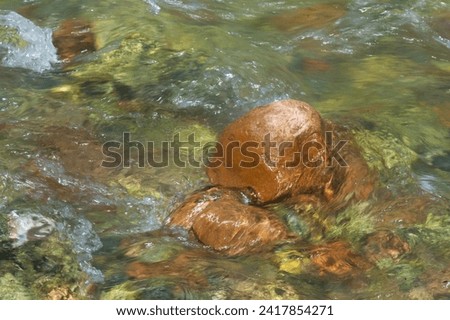 Orange-brown boulder in fast-flowing clear water of a stream. Photographed with long shutter speed. Motion blur