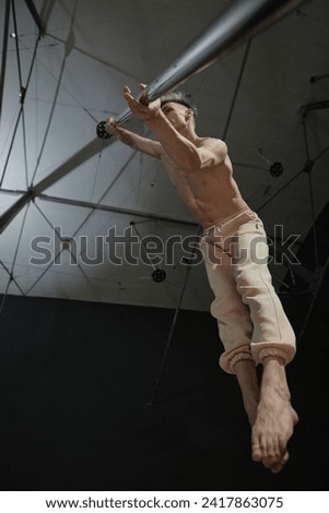 Vertical worms eye view at bare-chested man in air exercising dance moves in studio holding on to pylon with twisted grip