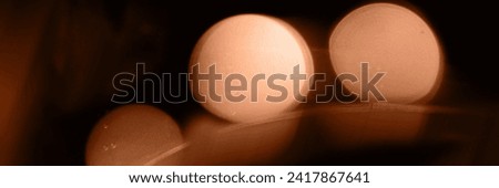 Blurry garland lights on a dark background. Festive Christmas and New Year background. Soft focus. Image toned in color of the year 2024 - Peach Fuzz