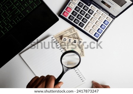 Debt word written on white office background with laptop, US dollar, diary and calculator on it.