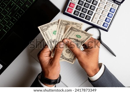 Businessman counting US dollars  on white office table with laptop and calculator  on it.