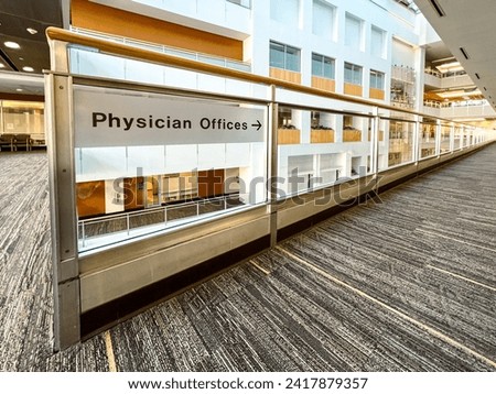 Transparent signage with arrow directing visitors to Physician Offices. Sign affixed to a balcony overlooking a modern office scene.