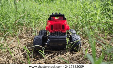 a small  offroad red colour car park on the grass,
toys offroad car