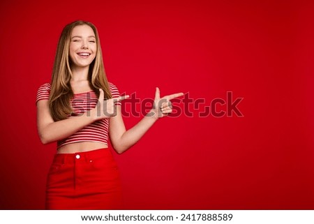 Photo of shiny tricky girl wear striped top winking showing two fingers empty space isolated red color background
