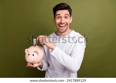 Photo of happiness when young man realizes he put last part money inside piggy bank to start business isolated on khaki color background