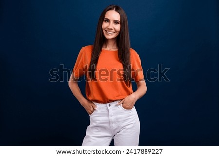 Photo of good mood adorable woman with straight hairdo dressed orange t-shirt keep arms in pockets isolated on dark blue background