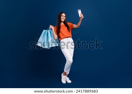 Full length photo of sweet shiny lady wear orange t-shirt holding bargains recording video vlog device isolated dark blue color background