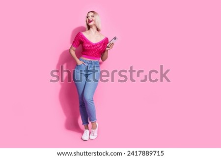 Full size photo of lovely nice woman dressed knit top denim pants look at sale empty space hold smartphone isolated on pink background
