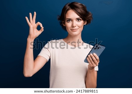 Photo portrait of attractive young woman hold device showing okey sign dressed stylish white clothes isolated on dark blue color background
