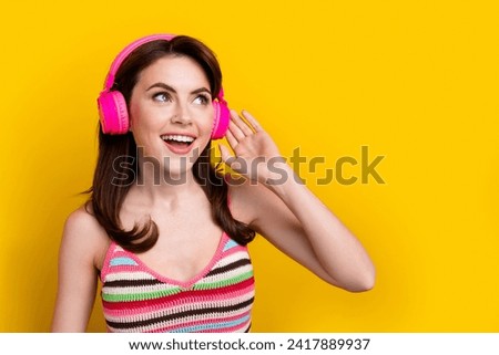Photo of nice girl with stylish hairdo dressed striped top touch headphones look empty space isolated on bright yellow color background