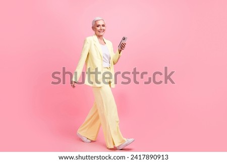 Full size photo of clever satisfied woman dressed yellow suit go to empty space holding smartphone isolated on pink color background