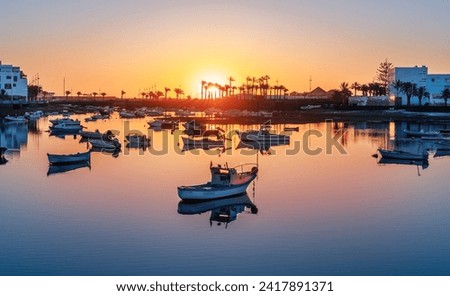 Lanzarote sunrise over Arrecife featuring a lone boat on calm waters. The capital's coastal creating a tranquil scene on Charco de San Gines lake.  Royalty-Free Stock Photo #2417891371